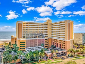 A large hotel with multiple floors, a rooftop pool, and a view of the ocean.
