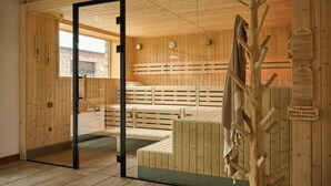 A sauna room with wooden benches, a glass door entrance, and a sign in German. - WANGERLAND RESORT (Wangerland)