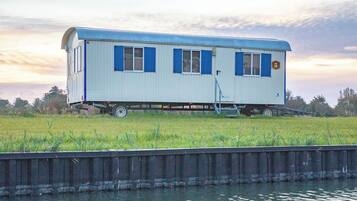 A stationary houseboat with a flat roof, a small deck, and a ladder.