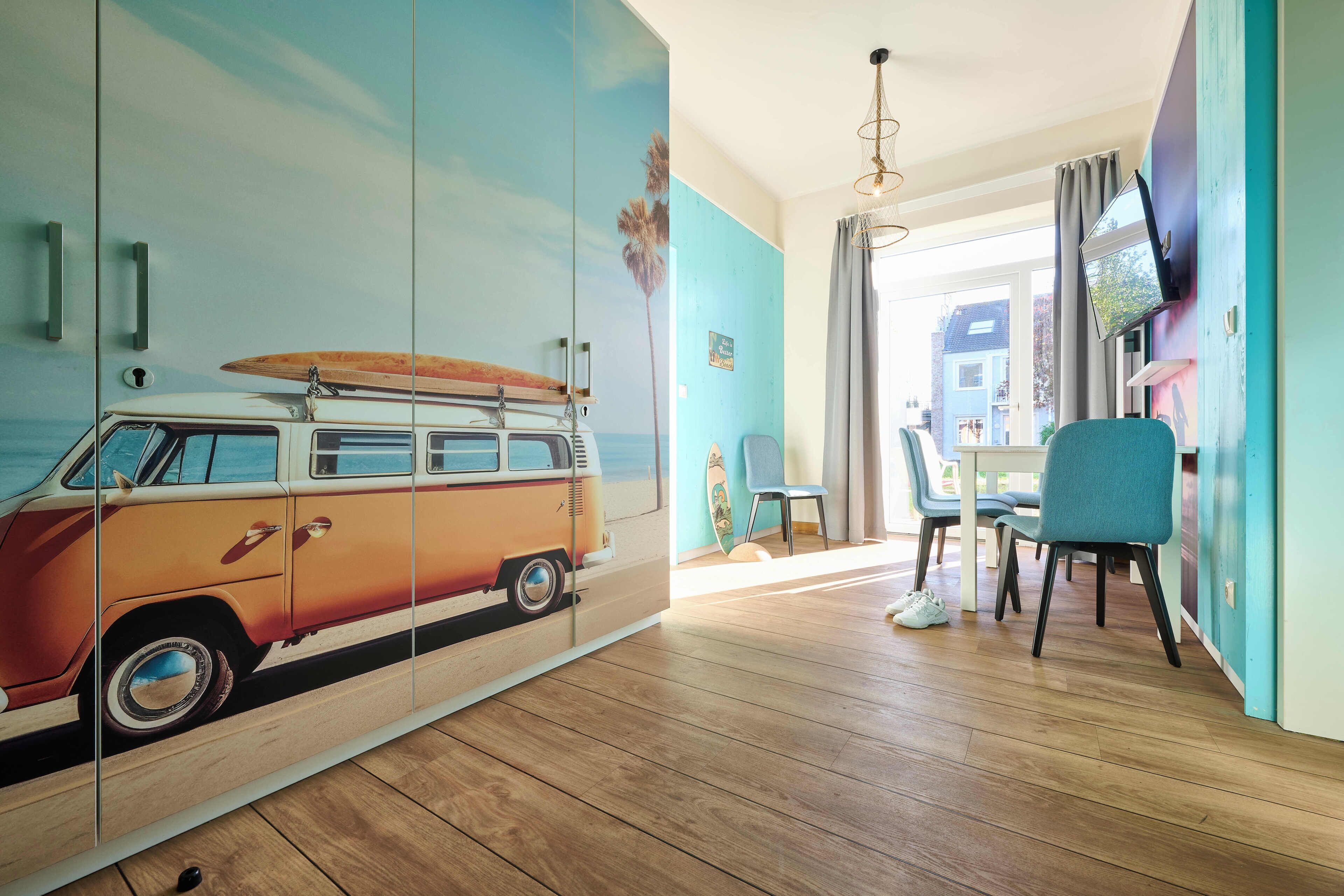 Une pièce décorée d’une fresque représentant un fourgon, une table à manger avec des chaises et un téléviseur fixé au mur.