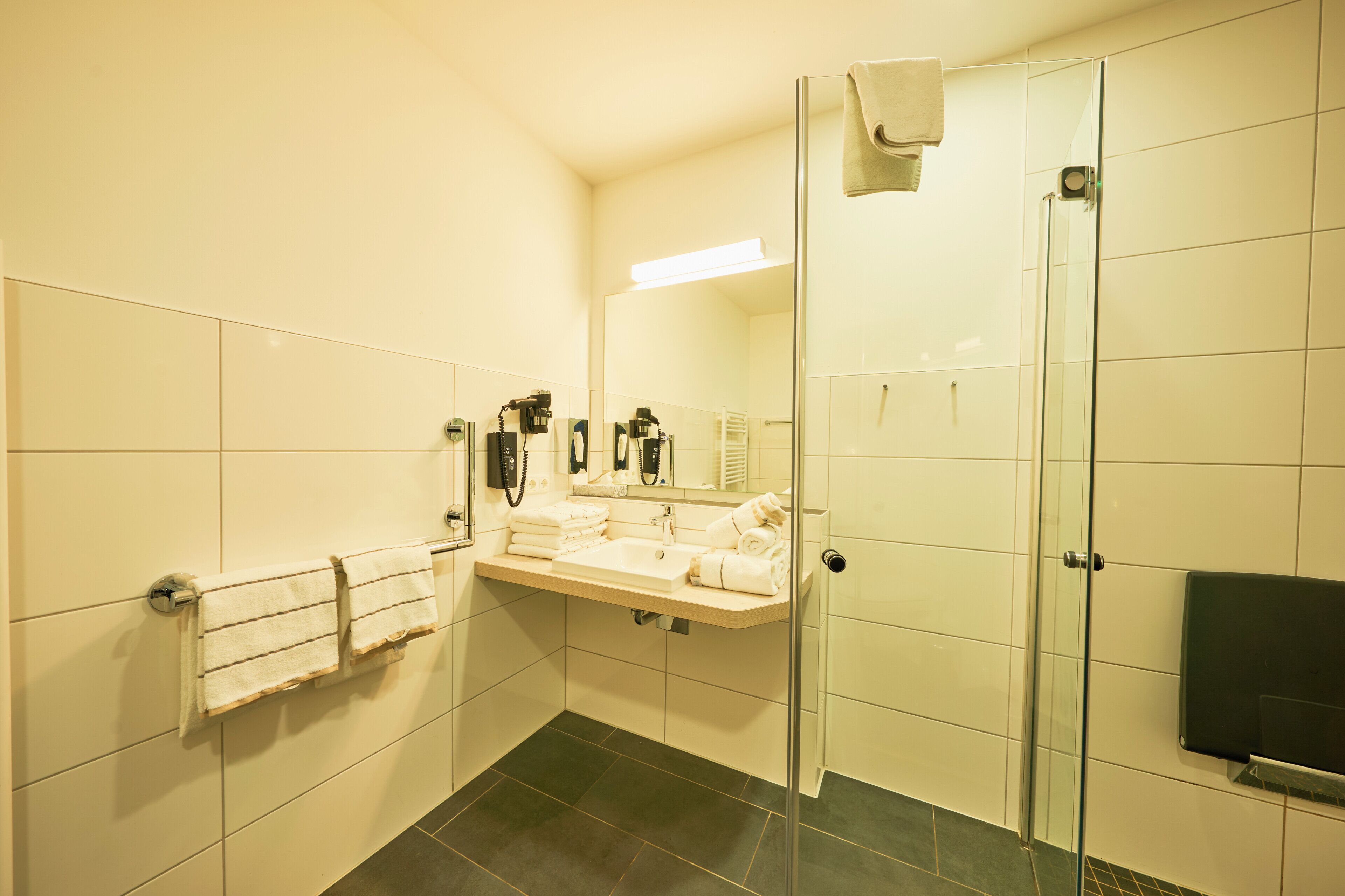 A modern bathroom with a glass shower enclosure, a sink with a towel rack, and a mirror.