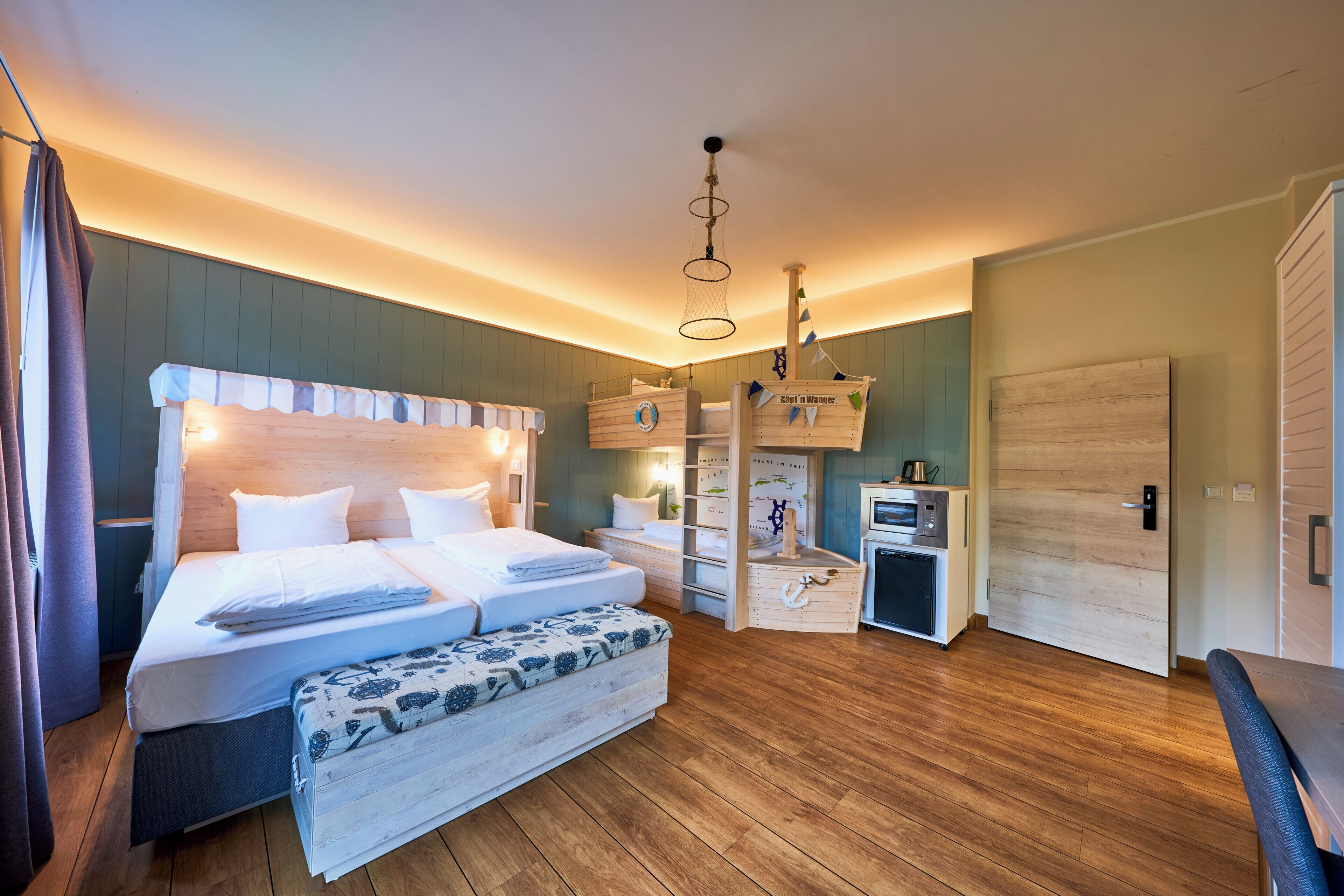 A room with a double bed, a desk, a small kitchenette, and a wardrobe.