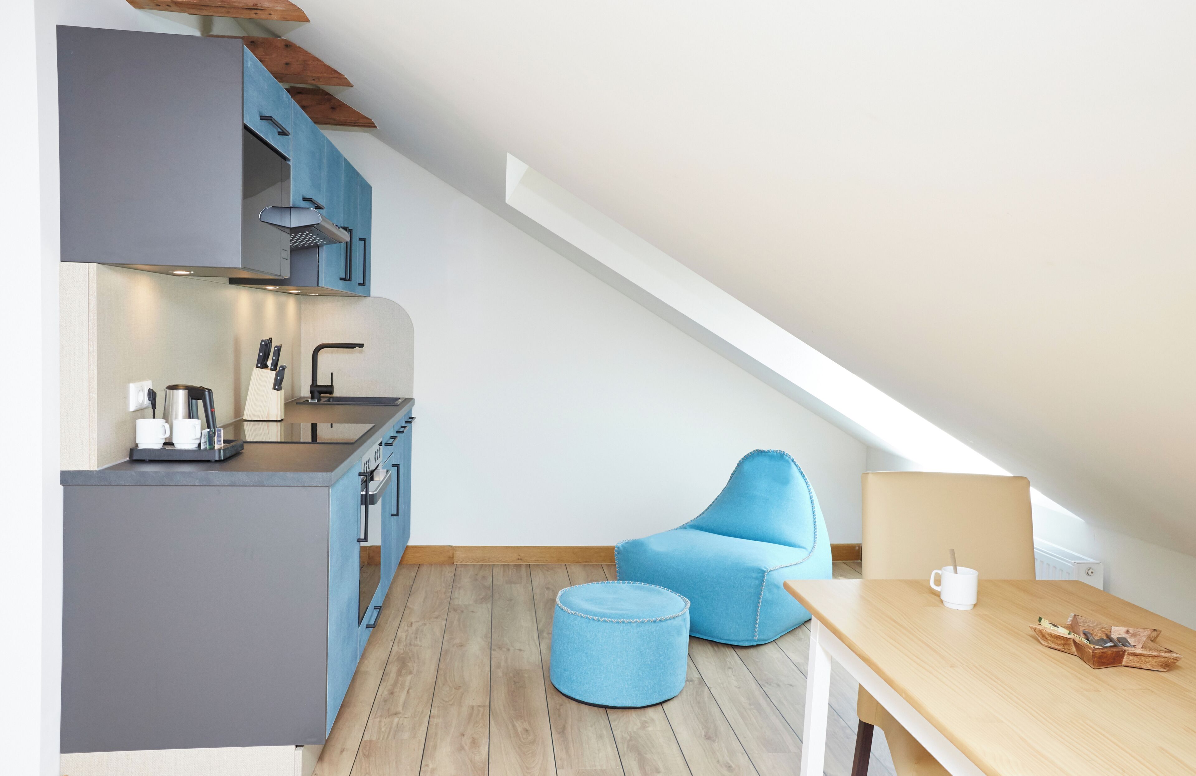 Eine kompakte Küche mit modernen Geräten, ein Essbereich mit einem Holztisch und einem blauen Stuhl.