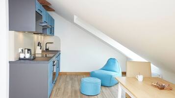 Eine kompakte Küche mit modernen Geräten, ein Essbereich mit einem Holztisch und einem blauen Stuhl.