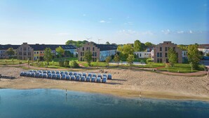 A lakeside hotel with multiple buildings, a sandy beach, and rows of sun loungers. - WANGERLAND RESORT (Wangerland)