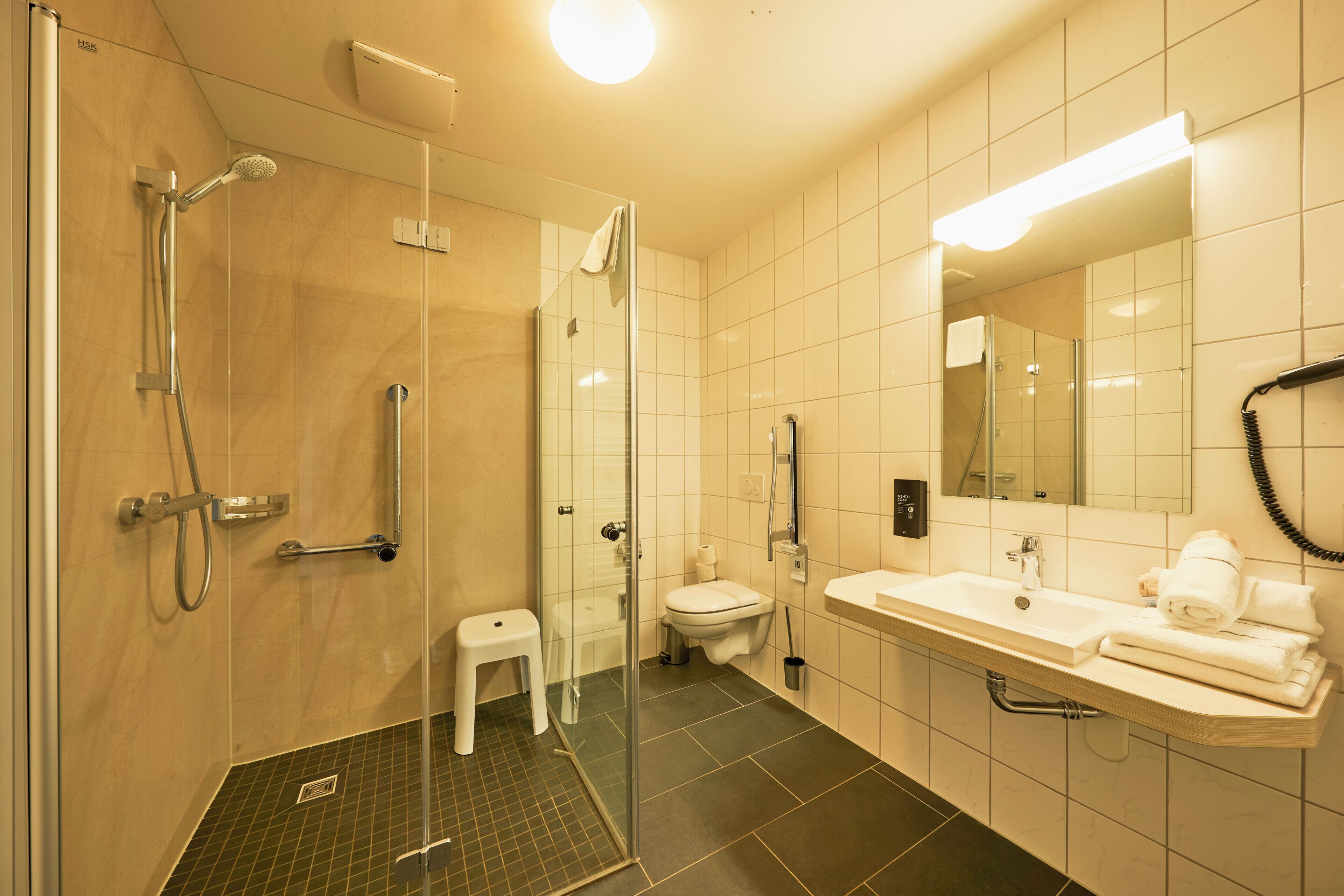 Un baño moderno con cabina de ducha de vidrio, un inodoro blanco y un lavamanos con toallas.