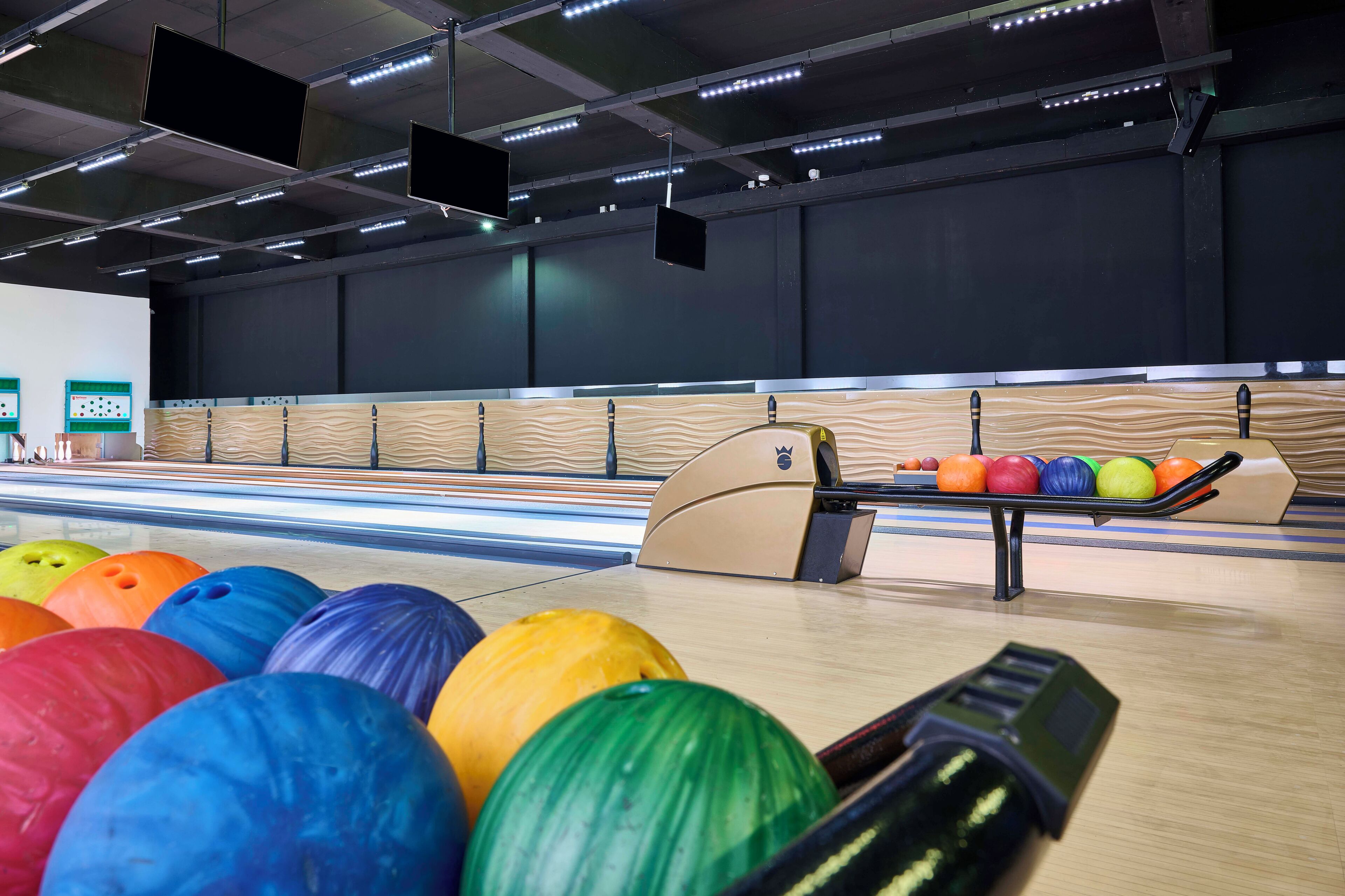 A bowling alley with multiple lanes, colorful bowling balls, and overhead lighting.