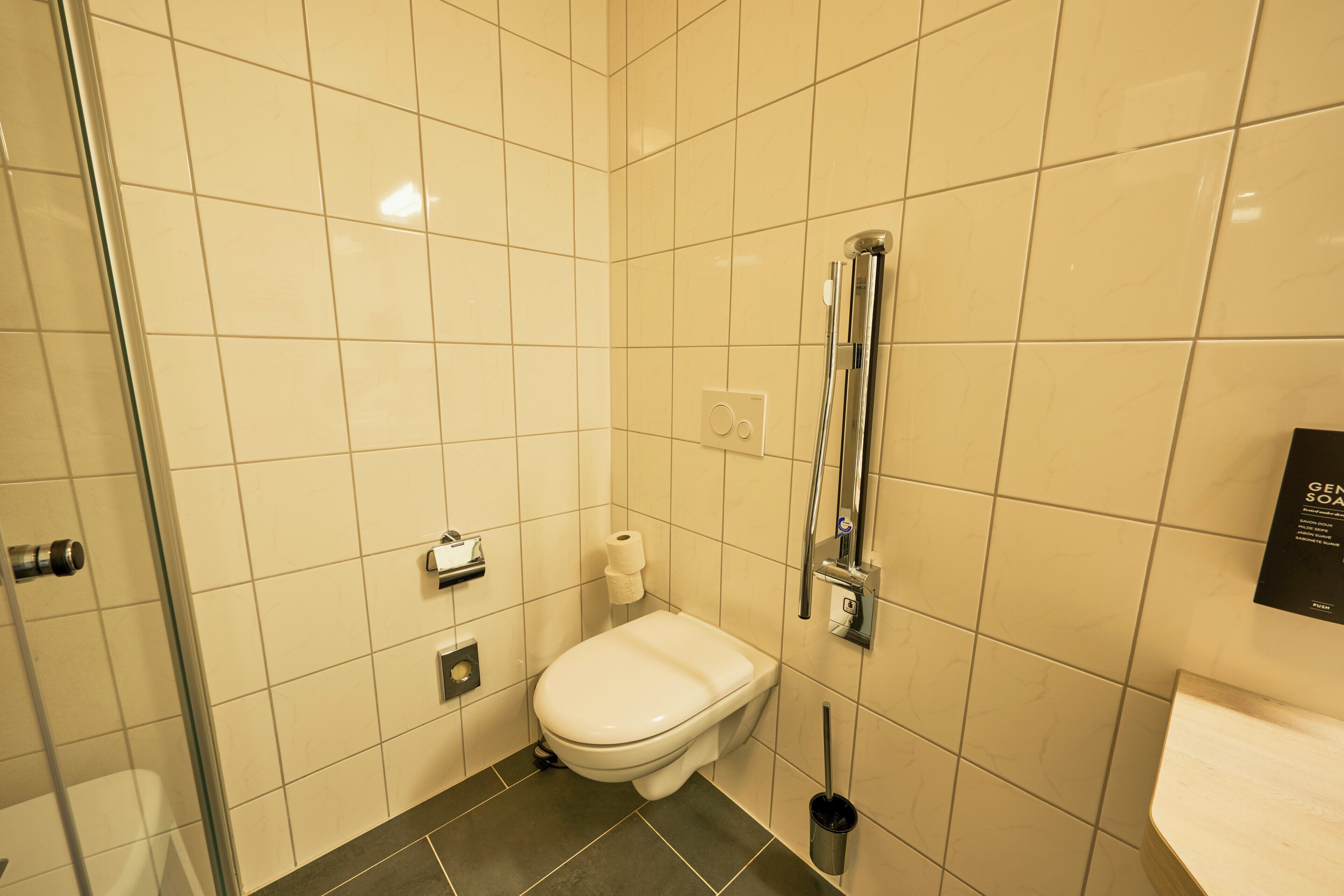 Une salle de bain comprenant des toilettes, un bidet, une douche avec un pommeau de douche amovible et un porte-rouleau de papier toilette.
