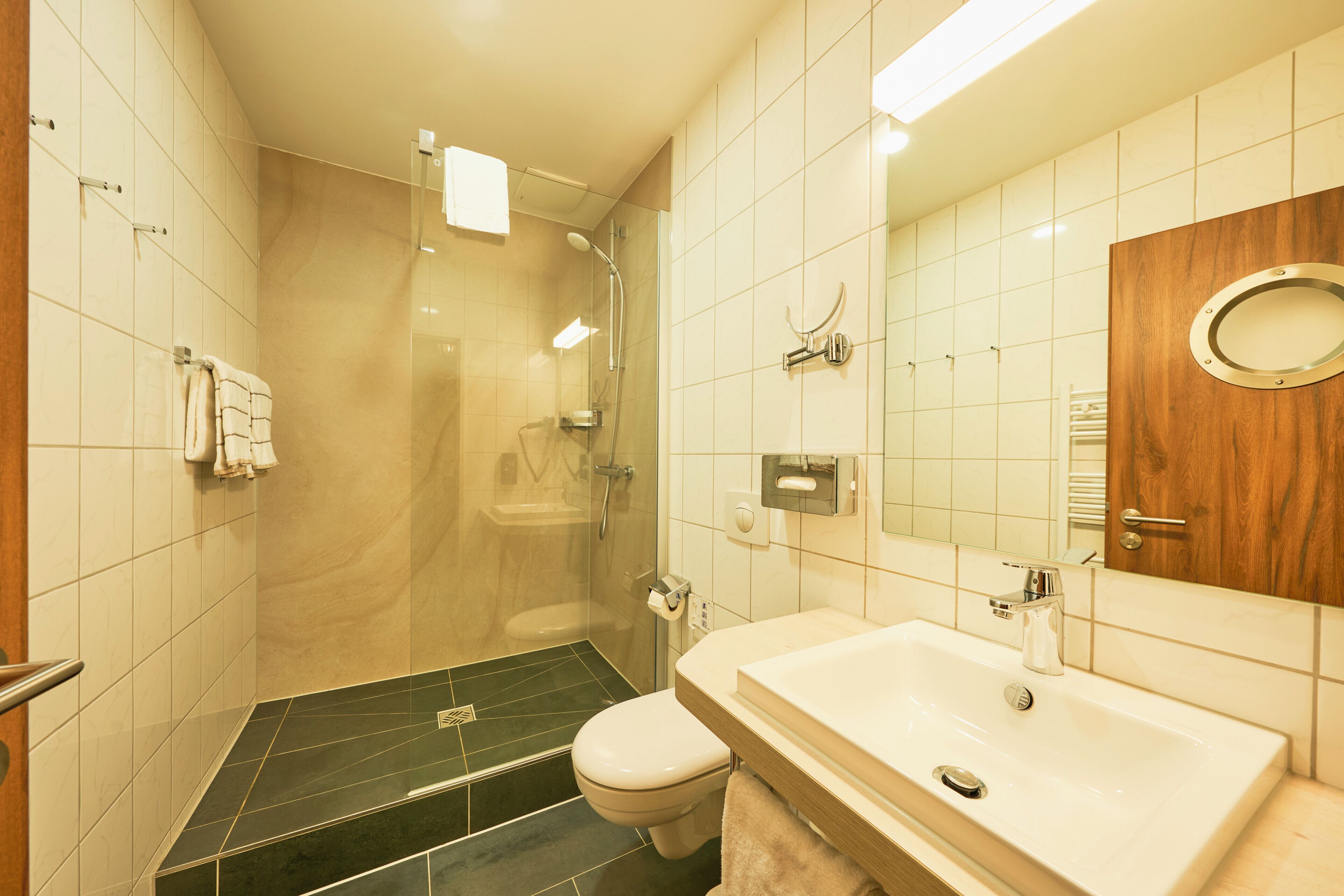 A bathroom with a shower, toilet, sink, and mirror.