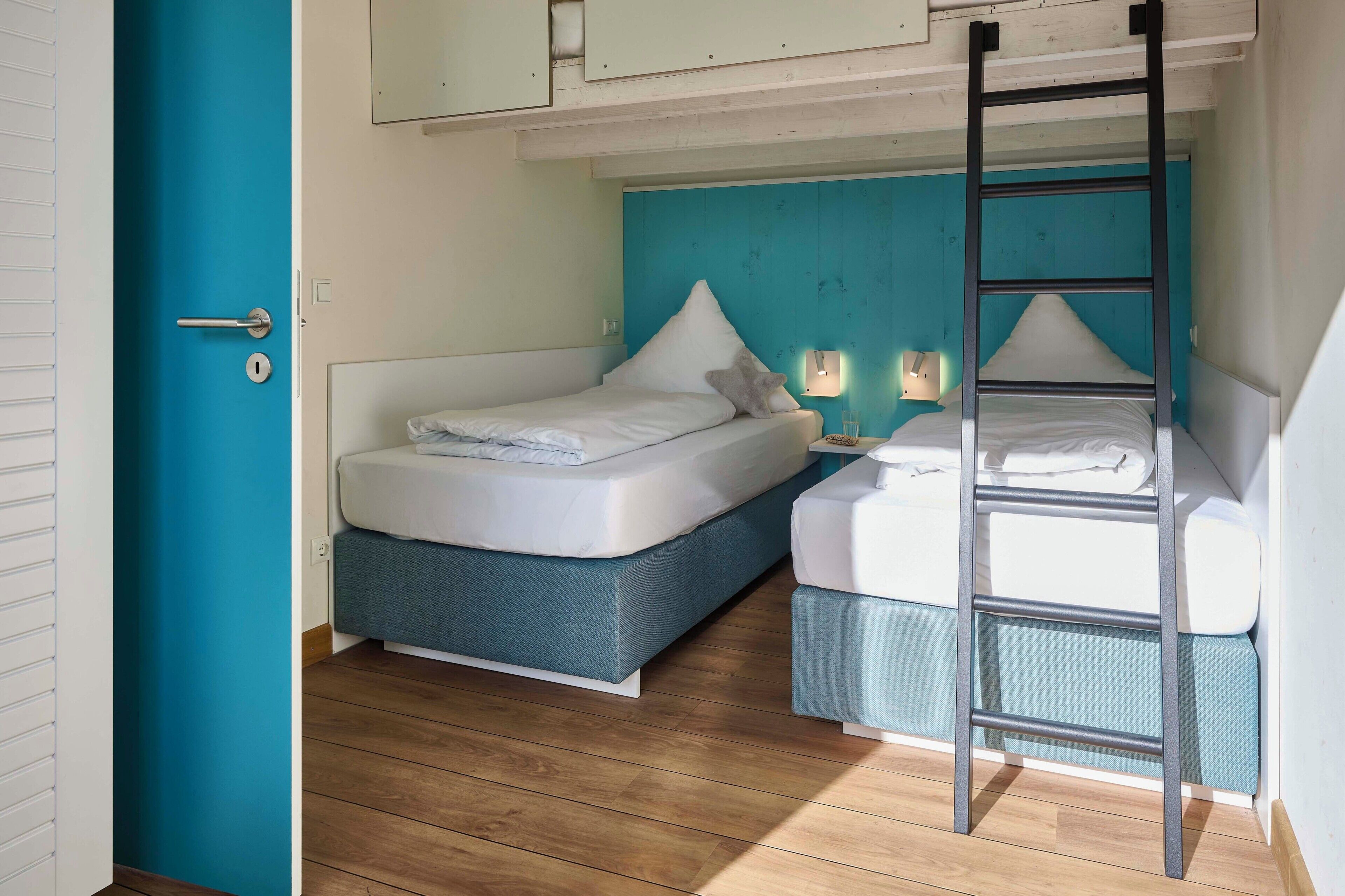 A room with a bunk bed, a ladder, a door, and a light fixture.