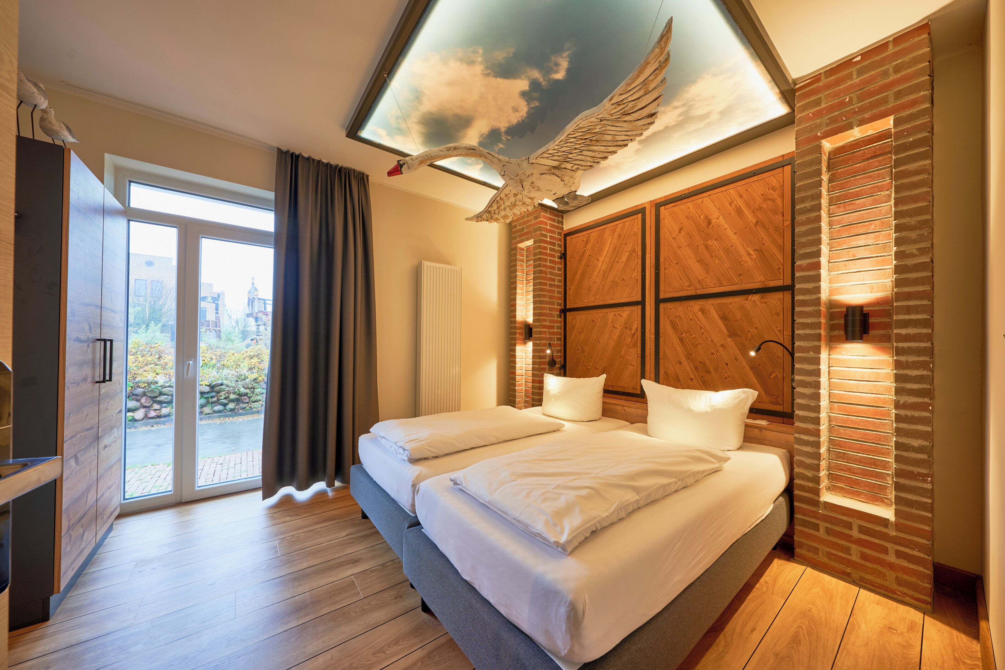 Habitación de hotel moderna con una cama grande, piso de madera, tragaluz con diseño de pájaro y vistas al exterior.