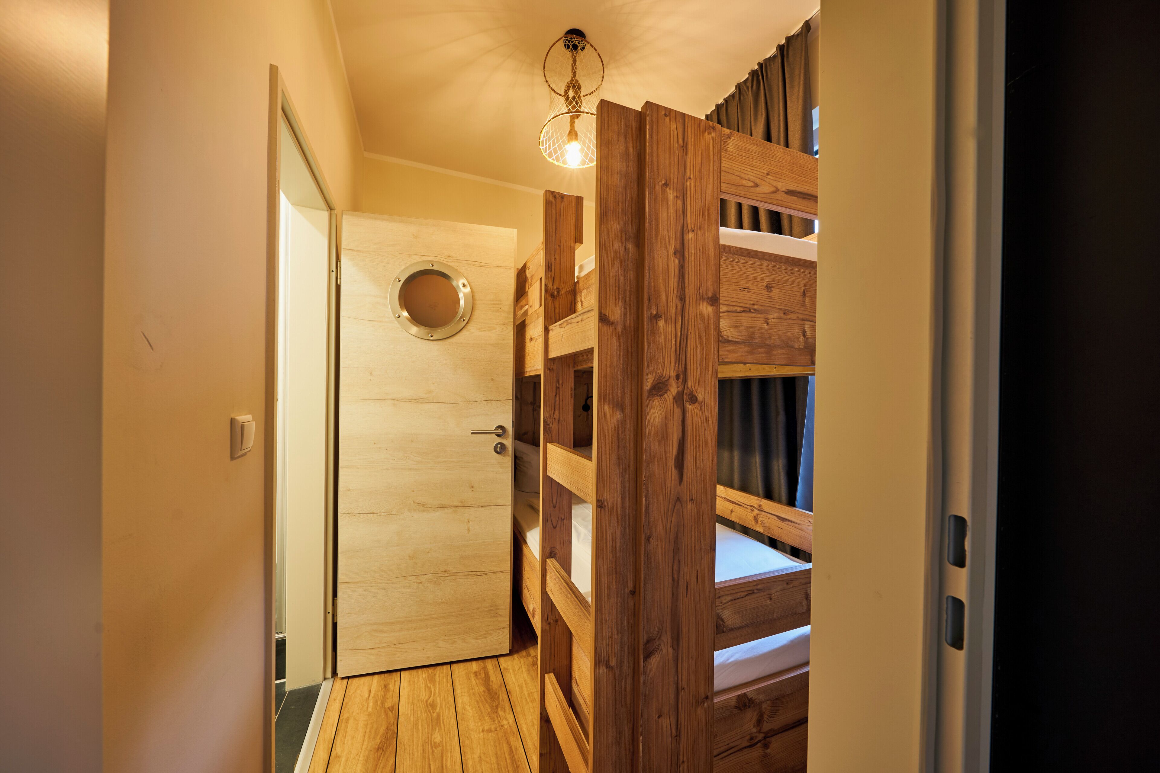 A wooden bunk bed with a circular window, a wooden door, and a light fixture.