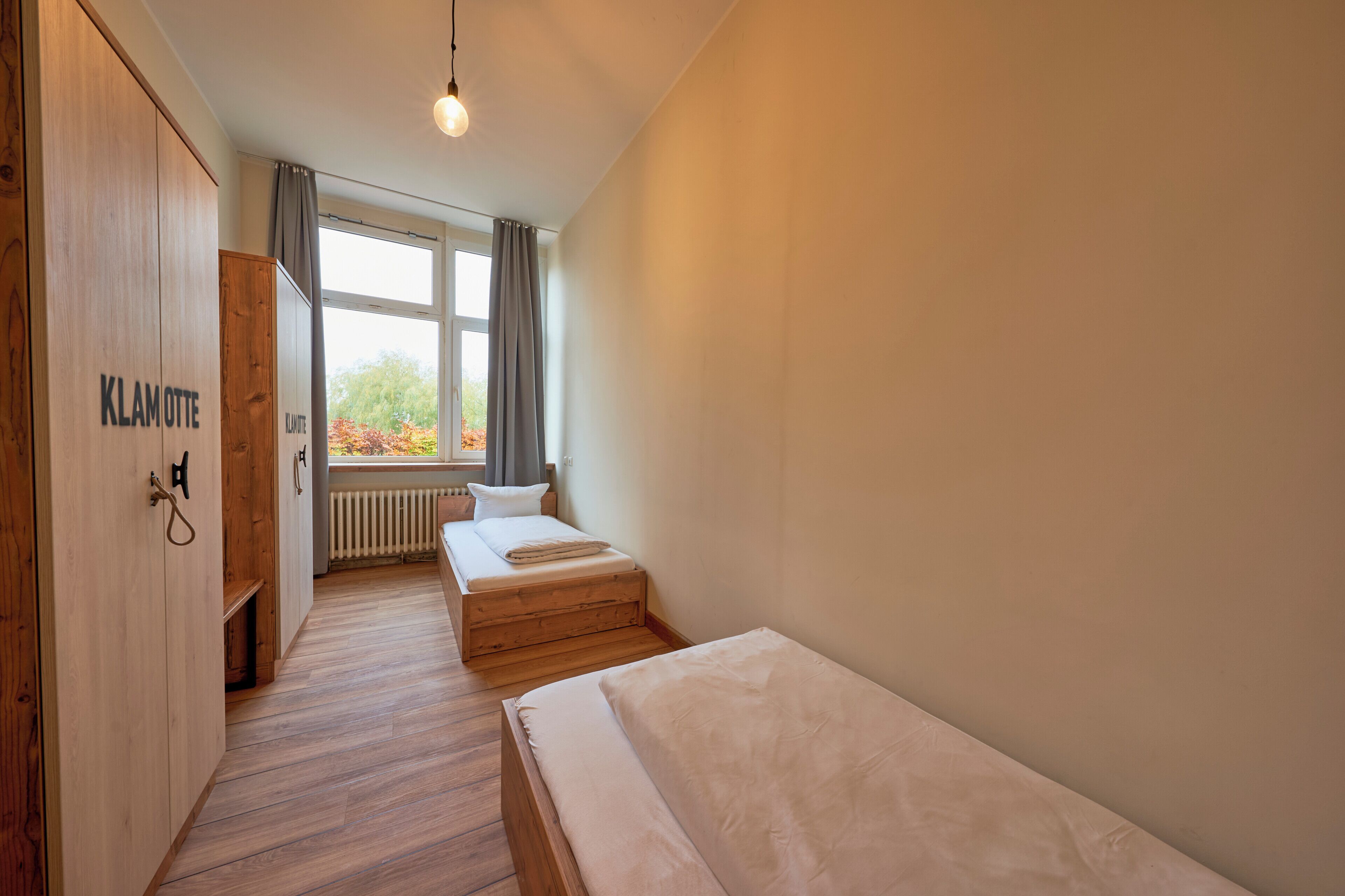 Una habitación con un armario de madera, una cama, un ventanal con vistas a árboles y un radiador.