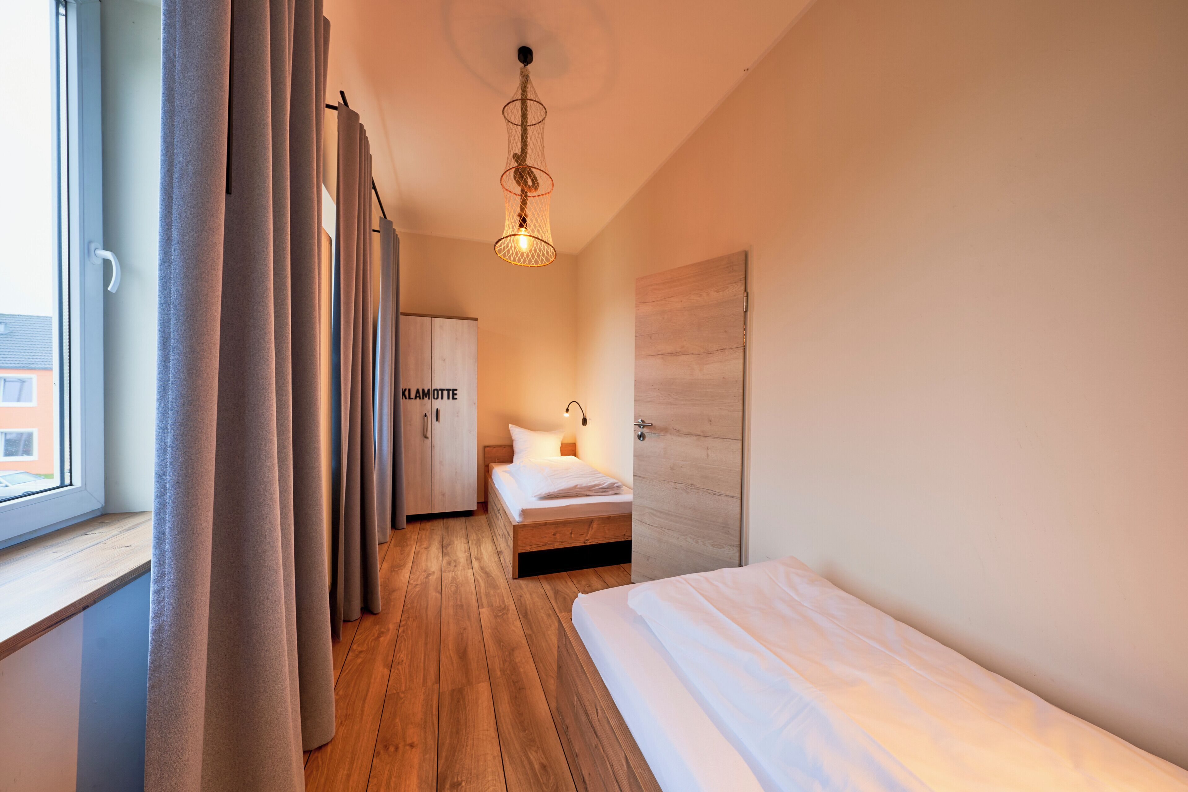 A modern hotel room with a wooden floor, a bed, a wardrobe, and a window with curtains.