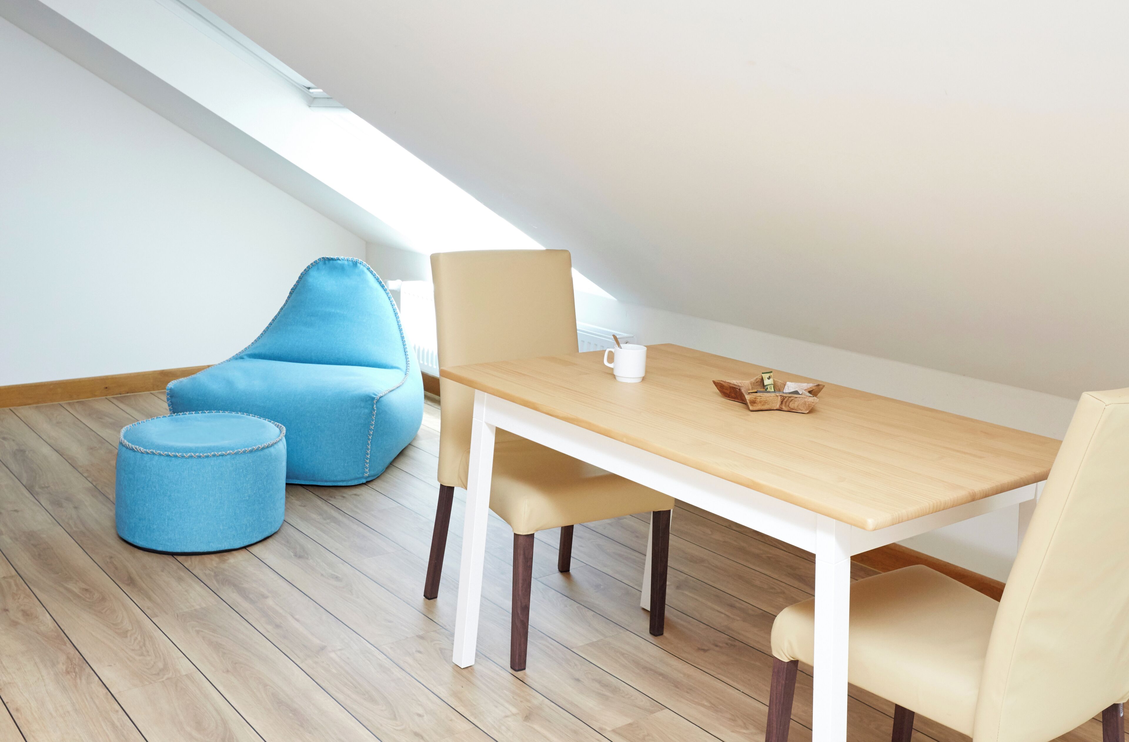 A dining area with a wooden table, two beige chairs, a blue ottoman, and a blue bean bag chair.