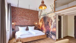 A modern hotel room with a brick wall, a large bed, a hanging light fixture, and a mural of a ship. - WANGERLAND RESORT (Wangerland)