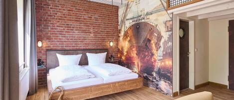 Ein modernes Hotelzimmer mit Backsteinwand, einem großen Bett, einer Pendelleuchte und einem Wandbild eines Schiffes.