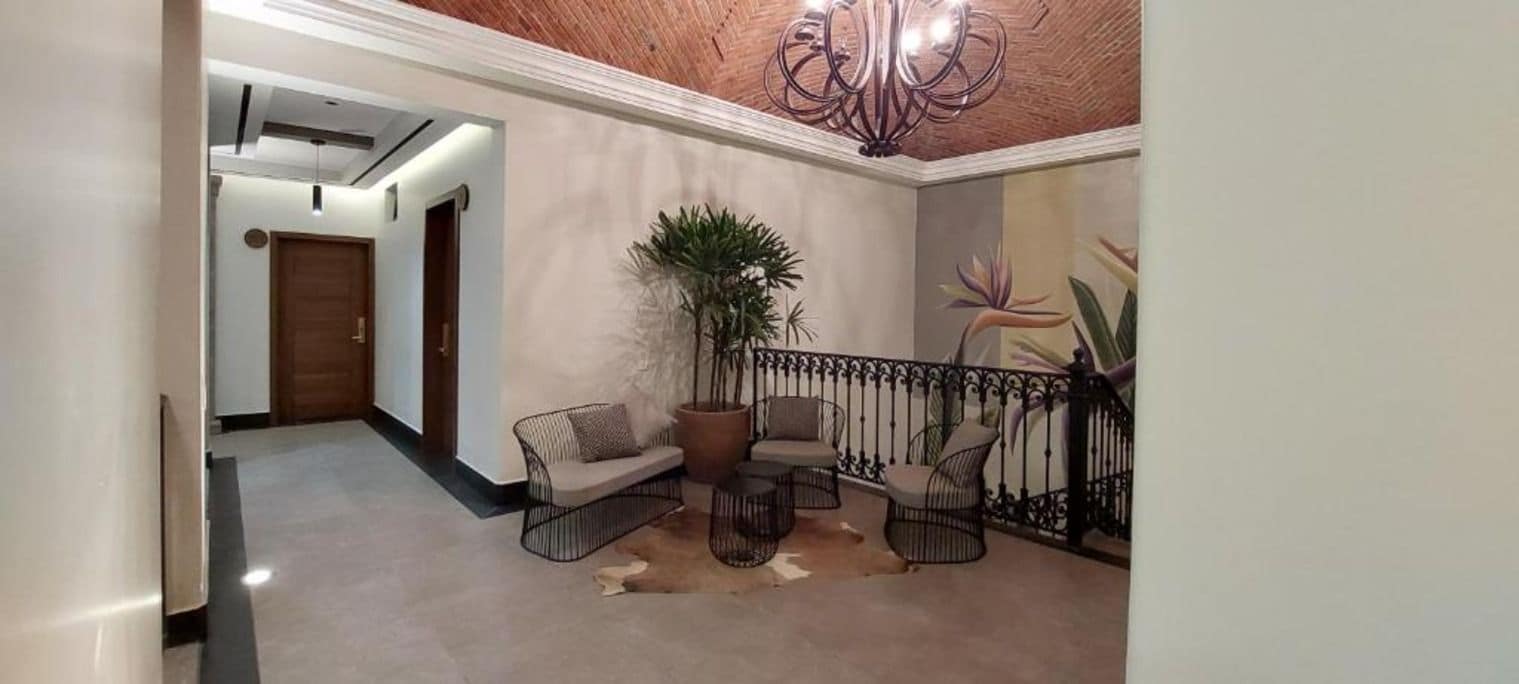 Un pasillo con techo, una puerta, una escalera y una zona de estar con sillas y una mesa.