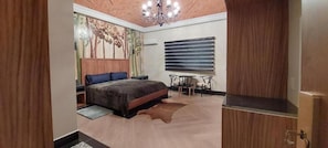 A bedroom with a bed, a desk, a chair, a chandelier, and a wall-mounted air conditioning unit.