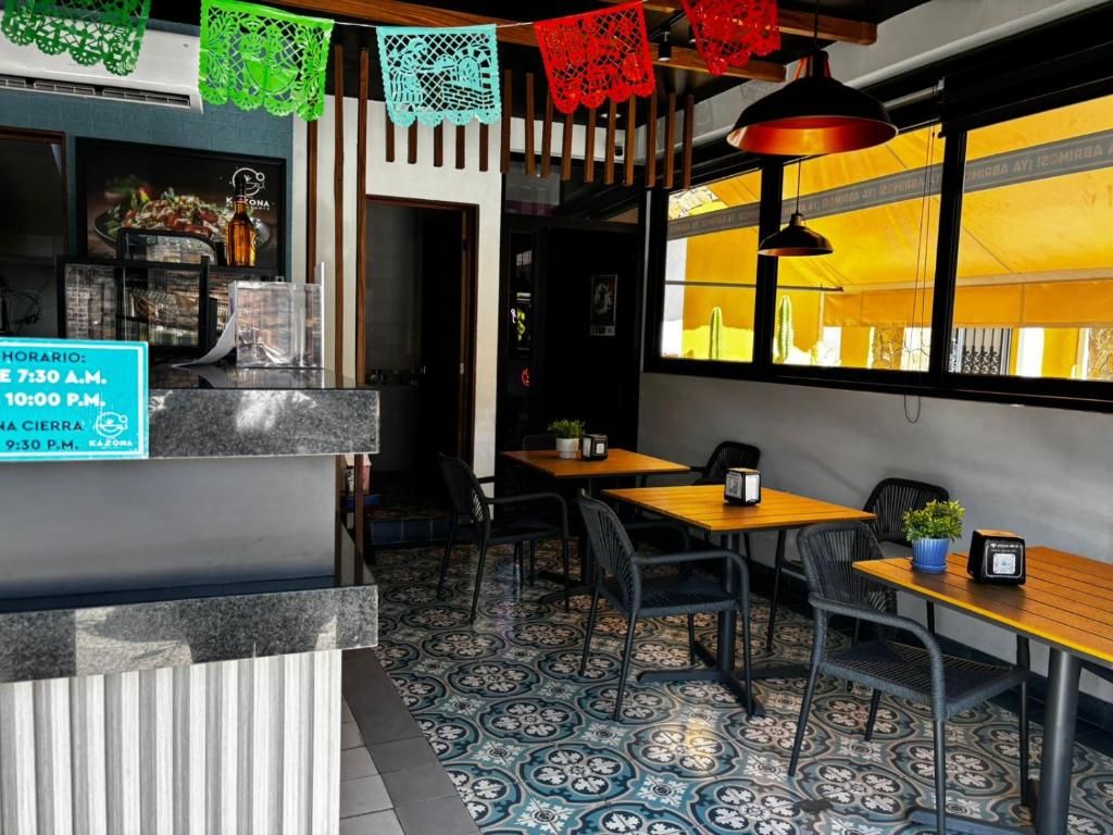 A restaurant interior with a counter, tables, chairs, and a view through a window.