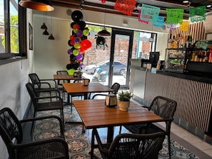 An indoor dining area with tables and chairs, a bar counter, and a view of the street outside.