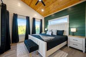Un dormitorio con cama, mesita de noche, banco y vistas al verdor exterior.