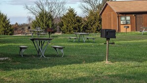 Eine begrünte Außenanlage mit Picknicktischen und Bänken, ein hölzernes Gebäude mit einem Briefkasten und Bäume im Hintergrund.