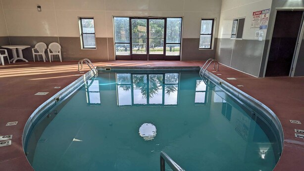 Ein Hallenbad mit klaren Glaswänden, einer Metallleiter und Blick ins Freie durch große Fenster.