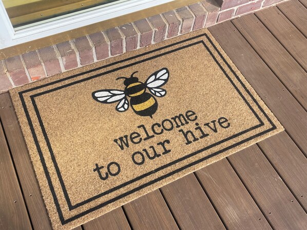 A welcome mat with a bee and the text "welcome to our hive" on a wooden deck. - The Honey Spot! Your Quiet retreat in Rineyville. (Rineyville)