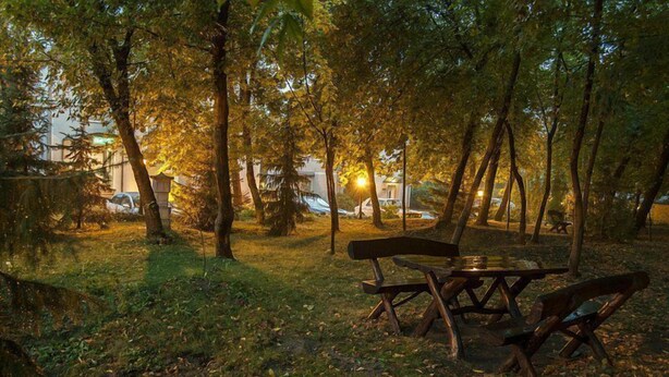 Una mesa de picnic y bancos en un parque, con árboles y un edificio al fondo.
