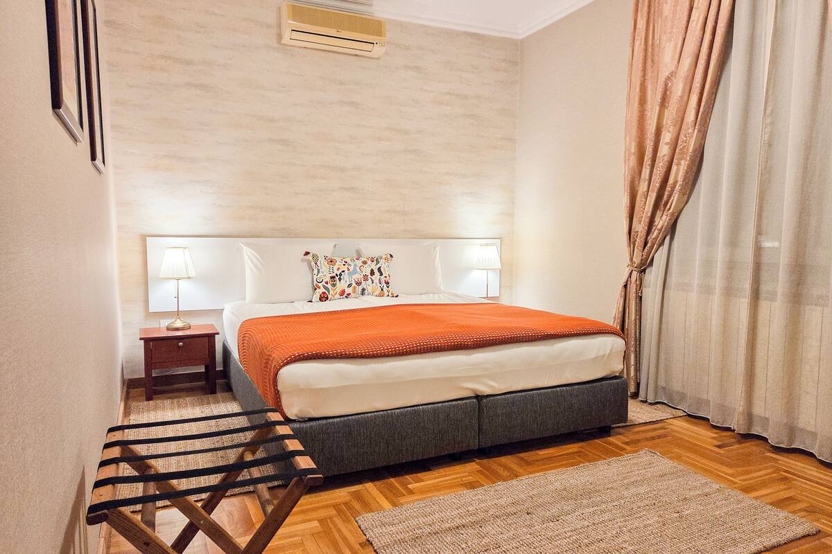 A hotel room with a bed, bedside tables, a lamp, a chair, a rug, and curtains.