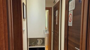 Un estrecho pasillo con puertas de madera, una pequeña zona de kitchenette y piso de madera.