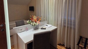 Habitación de hotel con escritorio, silla, aire acondicionado, cortinas y una pequeña mesa con un florero.