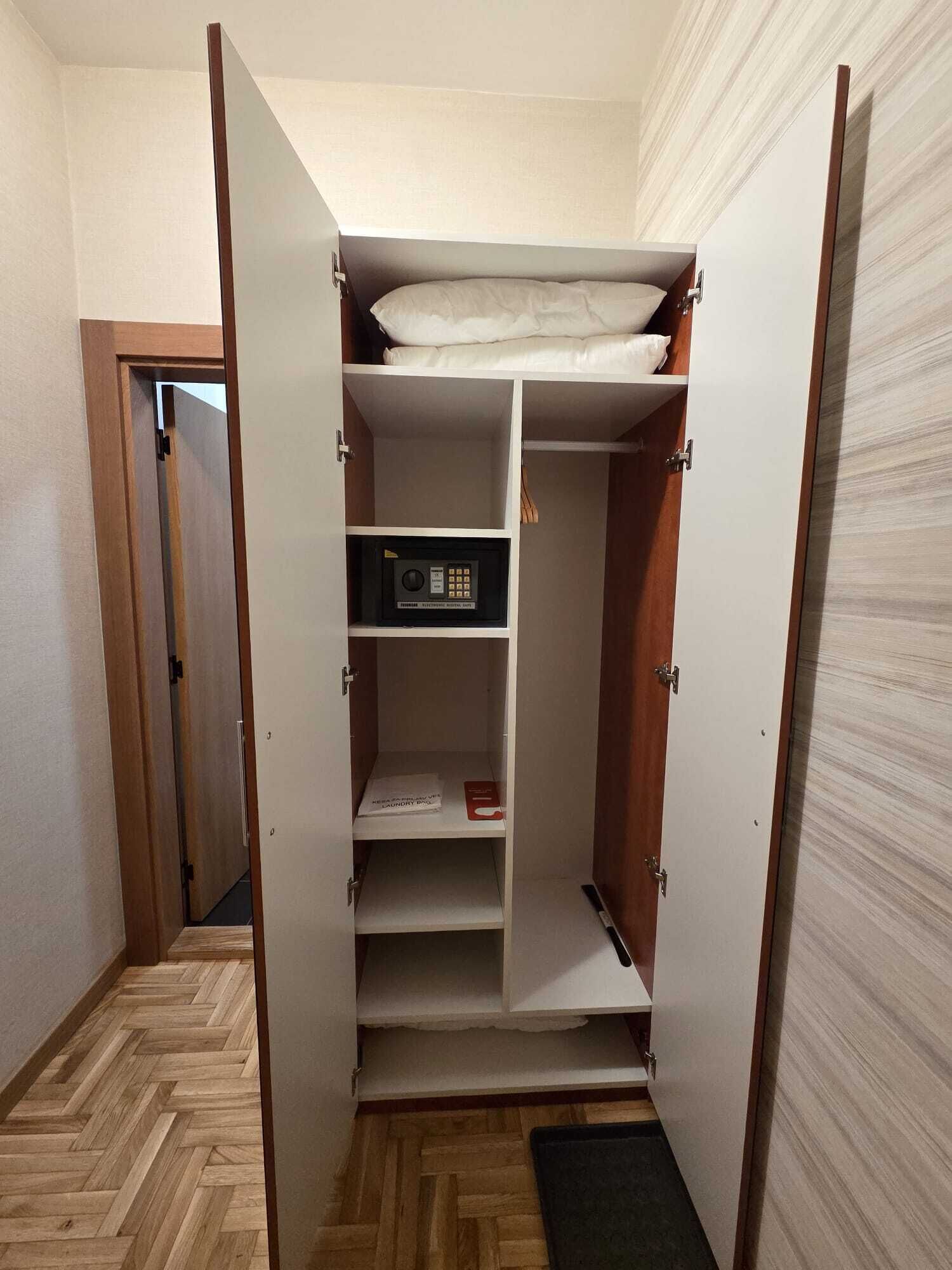 A walk-in closet with a bed at the top, a microwave, and a laundry basket.