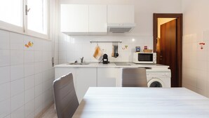 Cozinha compacta com armários brancos, micro-ondas, máquina de lavar e mesa de jantar.