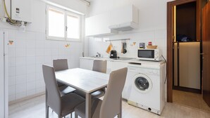 Cozinha compacta com área de refeições, máquina de lavar e micro-ondas.