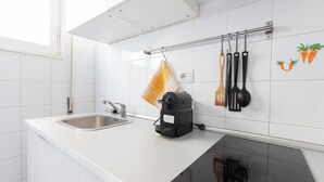 Uma cozinha moderna com azulejos brancos, uma pia de aço inoxidável, uma cafeteira preta e um fogão por indução preto.