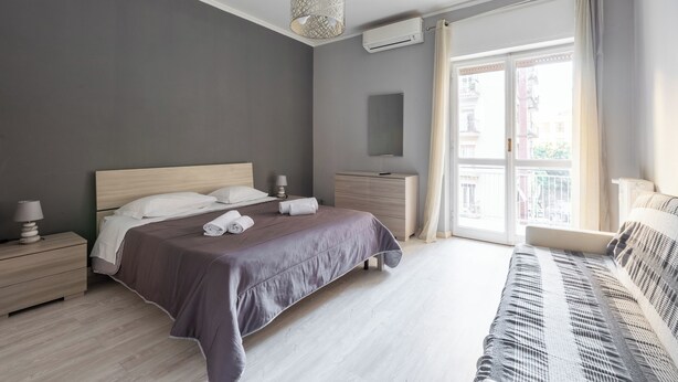 Quarto moderno com uma cama grande, mesas de cabeceira, penteadeira e um sofá.