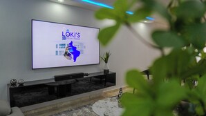 Una sala moderna con un televisor de pantalla plana grande montado en la pared, un mueble de entretenimiento negro debajo y una pequeña mesa redonda con objetos decorativos.