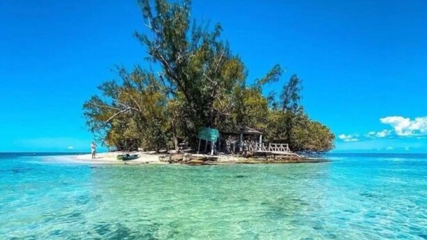 Un mar turquesa y transparente con una pequeña isla que presenta una estructura de madera y árboles exuberantes.