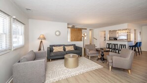 A modern living room with a sofa, armchairs, a coffee table, and a dining area with stools. - The Grand Elm Suite 2 Sleeps 6 (Covington)