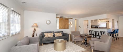 A modern living room with a sofa, armchairs, a coffee table, and a dining area with stools.