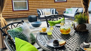A cozy outdoor seating area with wicker furniture, a round metal table, and a log cabin in the background. - NEW LISTING! Ski, Play, Stay @ The Lodge is loaded! Hot tub, BBQ, sleeps 10,  (Naches)