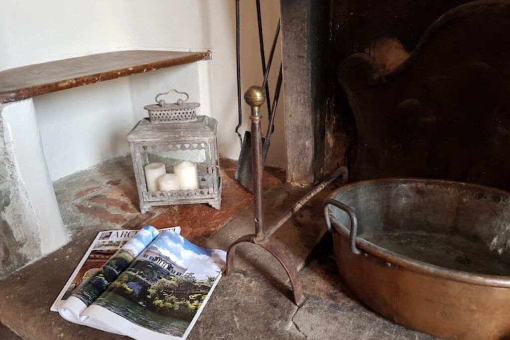 Een rustieke kamer met een houten plank, een metalen lantaarn, een koperen pan en een opgerold tijdschrift op de vloer.