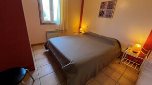 Une chambre à coucher comprenant un lit, une chaise, une fenêtre avec des rideaux, un radiateur et un élément de décoration murale.