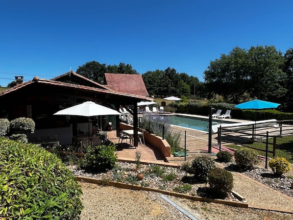 A pool area with lounge chairs and umbrellas, surrounded by a garden with gravel and plants.