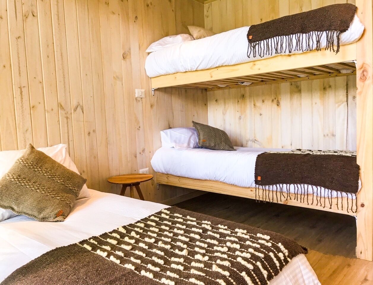 Una habitación de cabaña de madera con literas, una mesita redonda y una alfombra estampada.