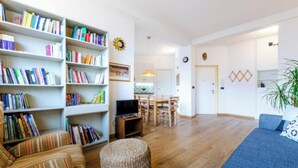 A living room with a sofa, a chair, a bookshelf, a dining table with chairs, and a television. - Modern Apartment with Panoramic City Views  (Milano)