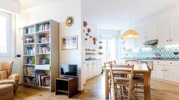 A spacious living room with a bookshelf, a television, and a dining area with wooden furniture. - Modern Apartment with Panoramic City Views  (Milano)