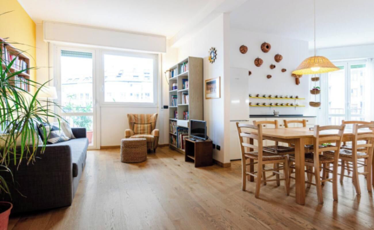 Una sala de estar acogedora con un sofá, una mesa de comedor con sillas, una estantería y un ventanal grande.
